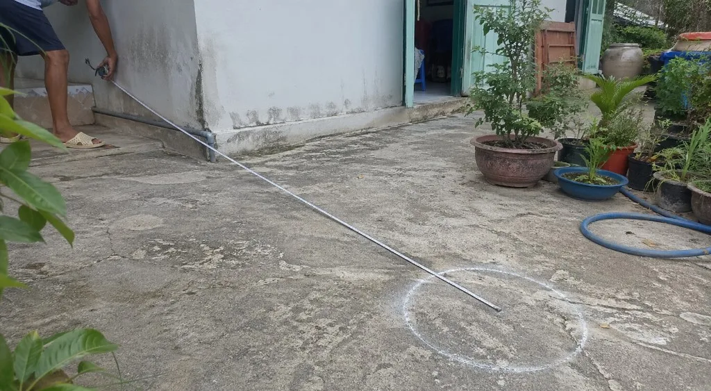 Thước dây kéo từ chân tường nhà tới vòng mốc khoan giếng vẽ bằng phấn trên nền bê tông